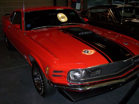 1972 Ford Ranchero - Front 3/4 view of a red muscle car with black stripes, parked indoors.