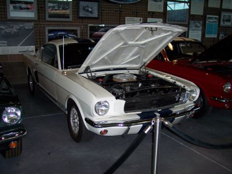 1972 Ford Ranchero - A white 1965 Ford Mustang with racing stripes and its hood open is displayed next to a red car.