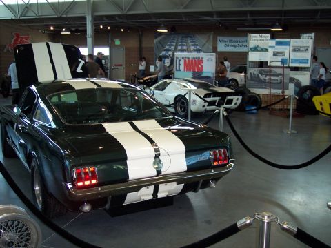 1972 Ford Ranchero - A dark green 1965 Ford Mustang fastback with white racing stripes is displayed indoors.