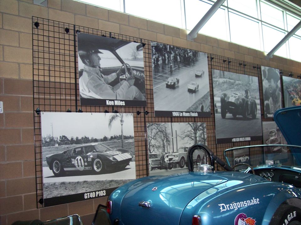 Teal Cobra roadster rear with 'Dragonsnake' lettering by wall of vintage racing photos