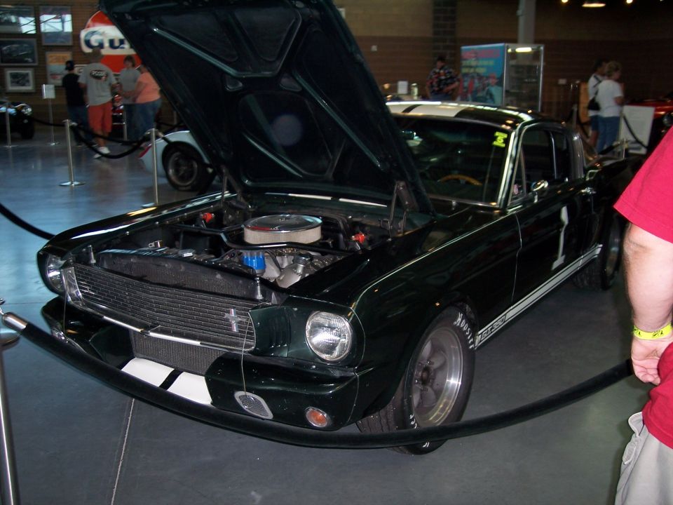 Dark green Mustang fastback with white stripes, number 1, hood up at an indoor car show
