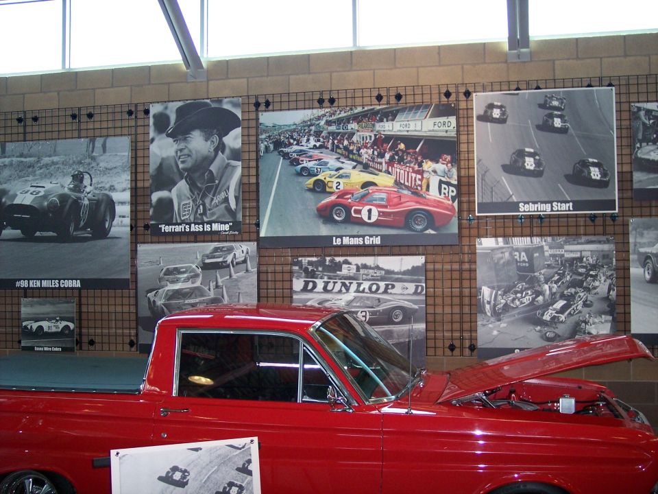 Red classic Ford with raised hood in front of racing photo wall exhibit