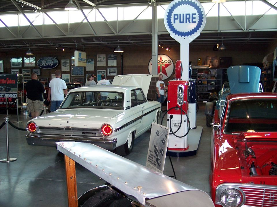 White vintage Ford sedan and red car on display in a museum with a red Pure gas pump.