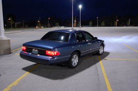 1985 Mercury Grand Marquis - Blue sedan parked in a lot at night, showing its rear end and taillights.