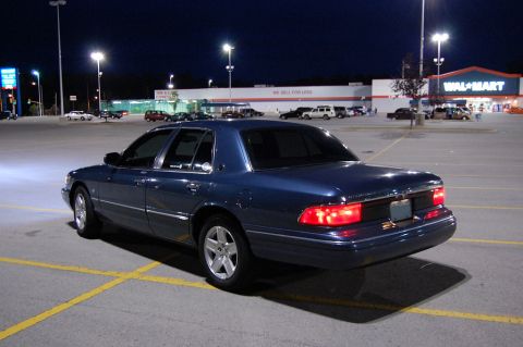 1985 Mercury Grand Marquis - A blue sedan is parked in a nearly empty parking lot outside a Walmart store after dark.