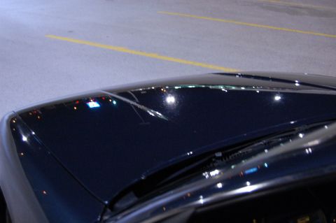 1985 Mercury Grand Marquis - The hood of a dark vehicle reflects city lights and parking lot markings.