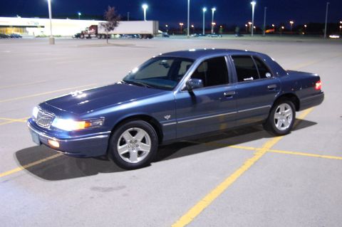 1985 Mercury Grand Marquis - This blue sedan is seen from a three-quarter front view in a parking lot after dark.
