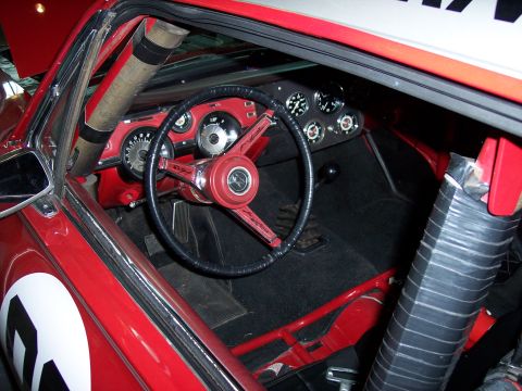 1972 Ford Ranchero - The interior of a red race car shows a custom steering wheel and dashboard gauges, with a roll cage visible.