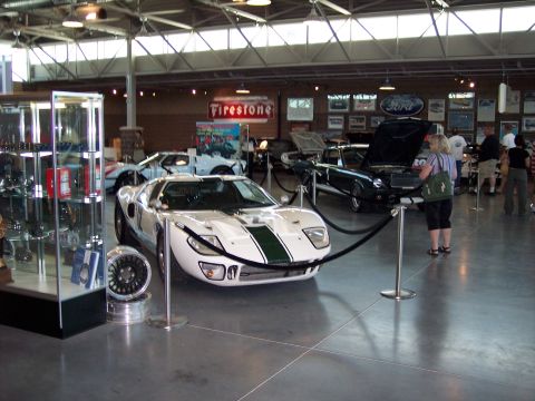 1972 Ford Ranchero - A white Ford GT40 with green racing stripes is displayed indoors, with other vehicles and memorabilia in the background.