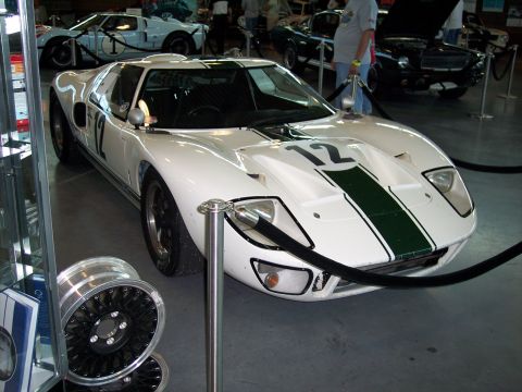 1972 Ford Ranchero - A white Ford GT40 race car with green stripes and the number 12 is displayed indoors, with other vehicles in the background.