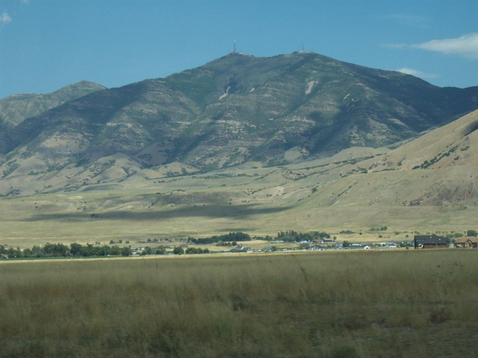 Mountain with towers above golden valley and rural buildings under blue sky