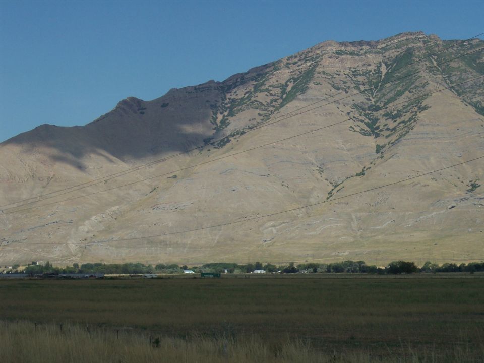 Barren mountain over golden field with power lines under blue sky