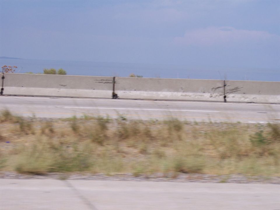 Empty highway with concrete barrier, dry grass, and a large lake on the horizon