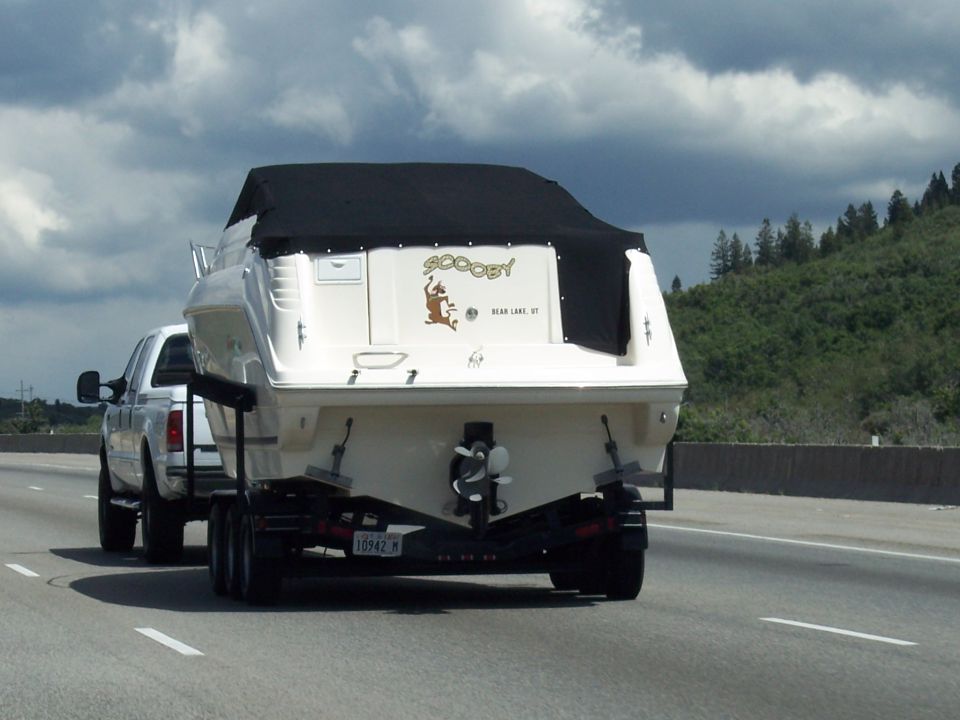 White pickup towing white "SCOOBY" boat on trailer down a highway.