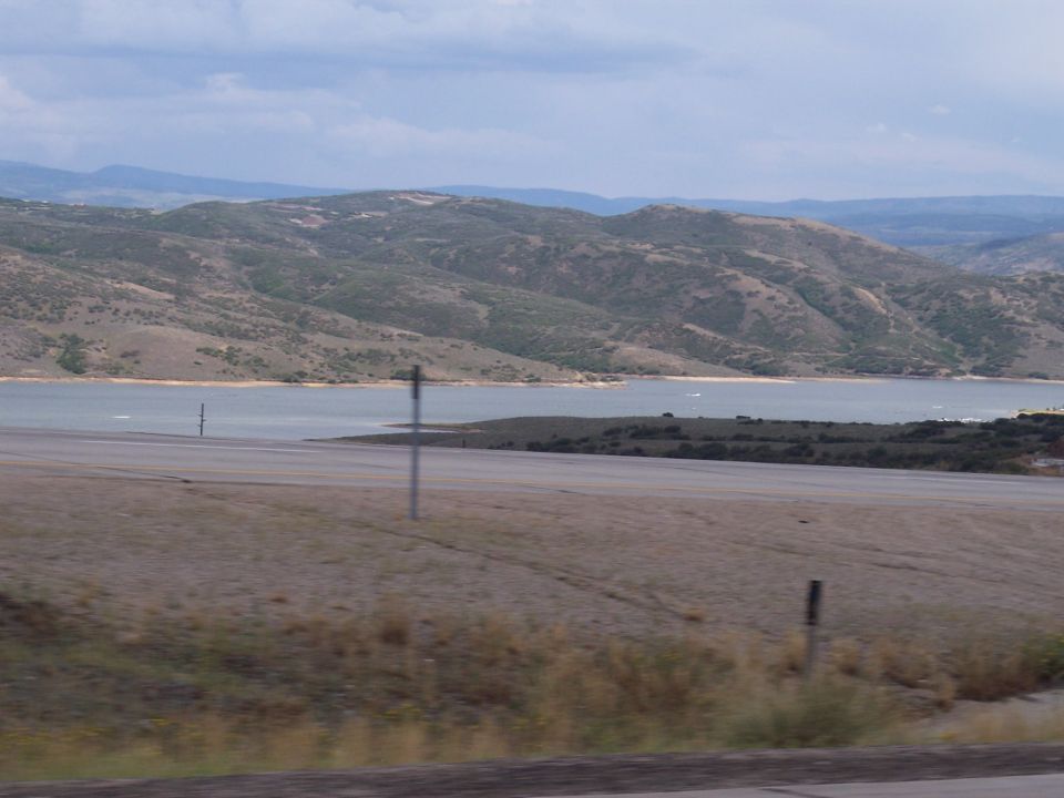 Hills and a lake behind a roadway with dry grass and a signpost under a cloudy sky
