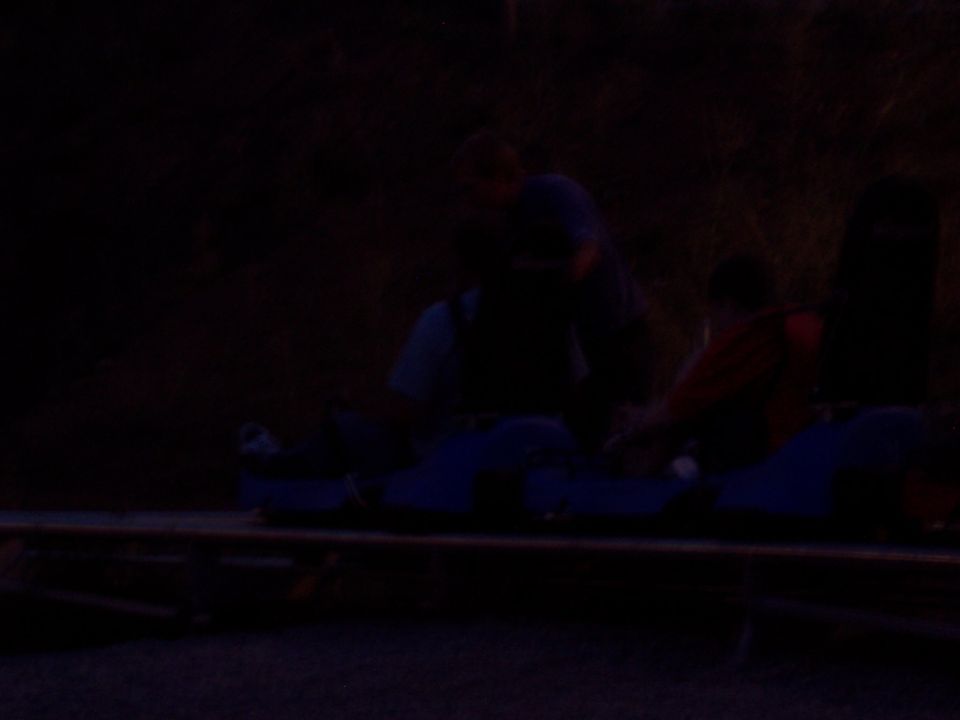 Dark image of people around a low open vehicle at dusk