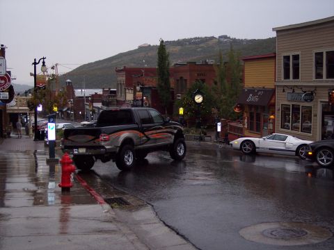 1972 Ford Ranchero - A black pickup truck with orange graphics is parked on a wet street in front of shops.