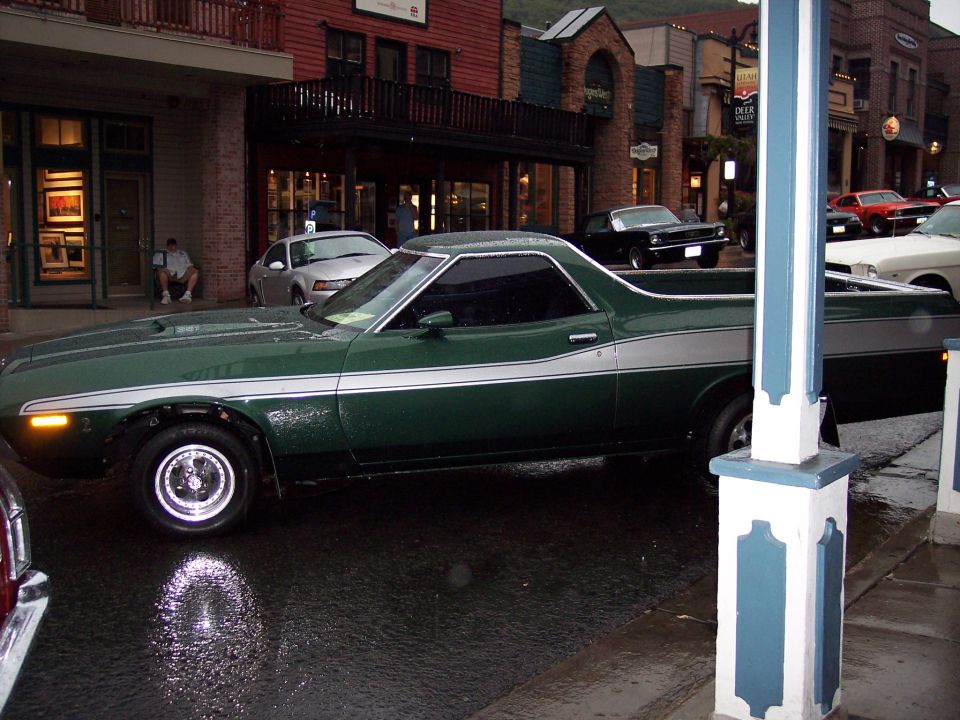 Dark green Ford Ranchero with white stripe parked in profile on a wet downtown street