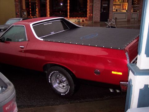 1972 Ford Ranchero - The side of a red pickup truck is visible, a black tonneau cover and chrome wheels.