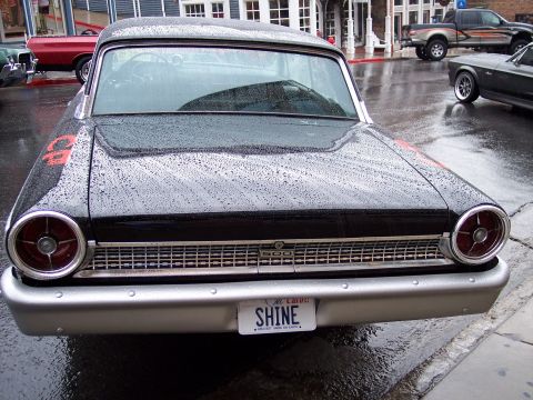 1972 Ford Ranchero - A black 1959 Ford Fairlane 500 with red accents is parked on a wet street, showing its front grille and license plate.