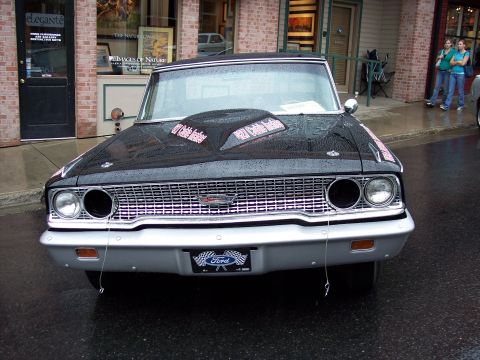 1972 Ford Ranchero - A black 1964 Ford Fairlane is parked on a wet street in front of shops.