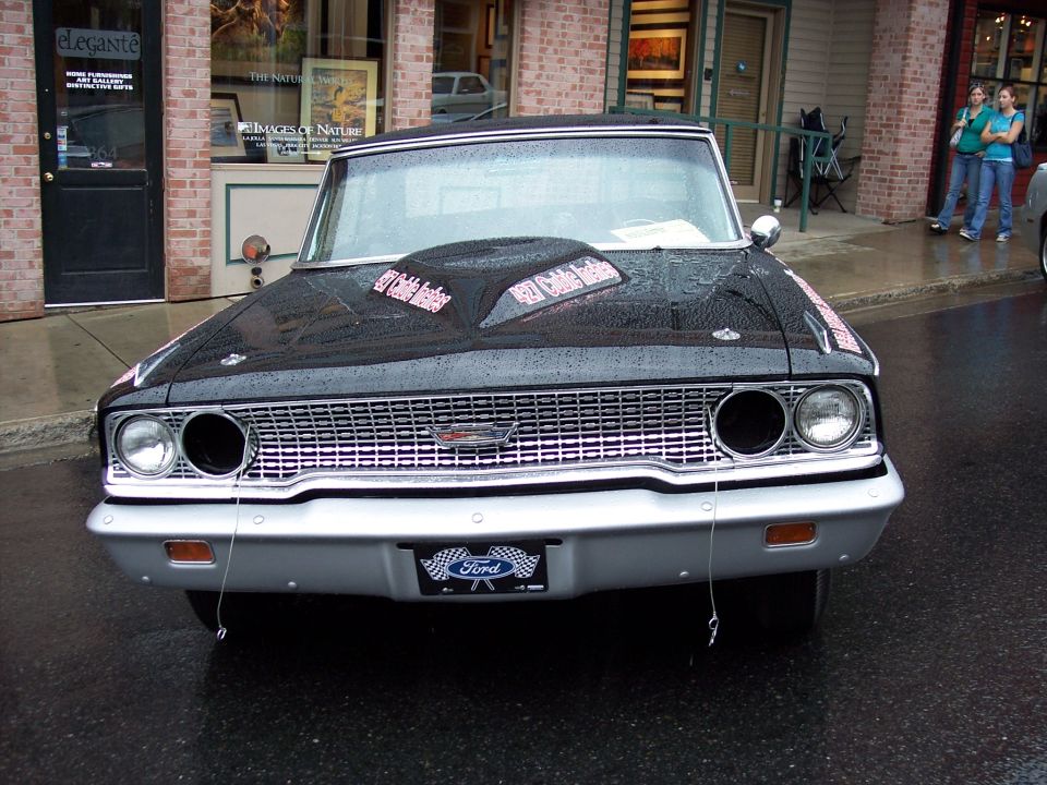 Black vintage Ford front end with chrome grille, dual headlights, and Ford plate on wet street