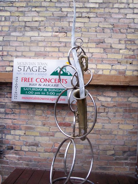 1972 Ford Ranchero - An abstract sculpture metal rings and saxophone components stands before a brick wall displaying a poster for 'Mountain Town Stages' free c…