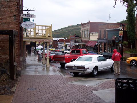 1972 Ford Ranchero - A white coupe is parked on a wet street in a town with shops and hills in the background.