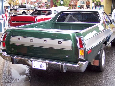 1972 Ford Ranchero - Rear view of a green 1972 Ford Ranchero GT parked on a wet street, with other vehicles in the background.