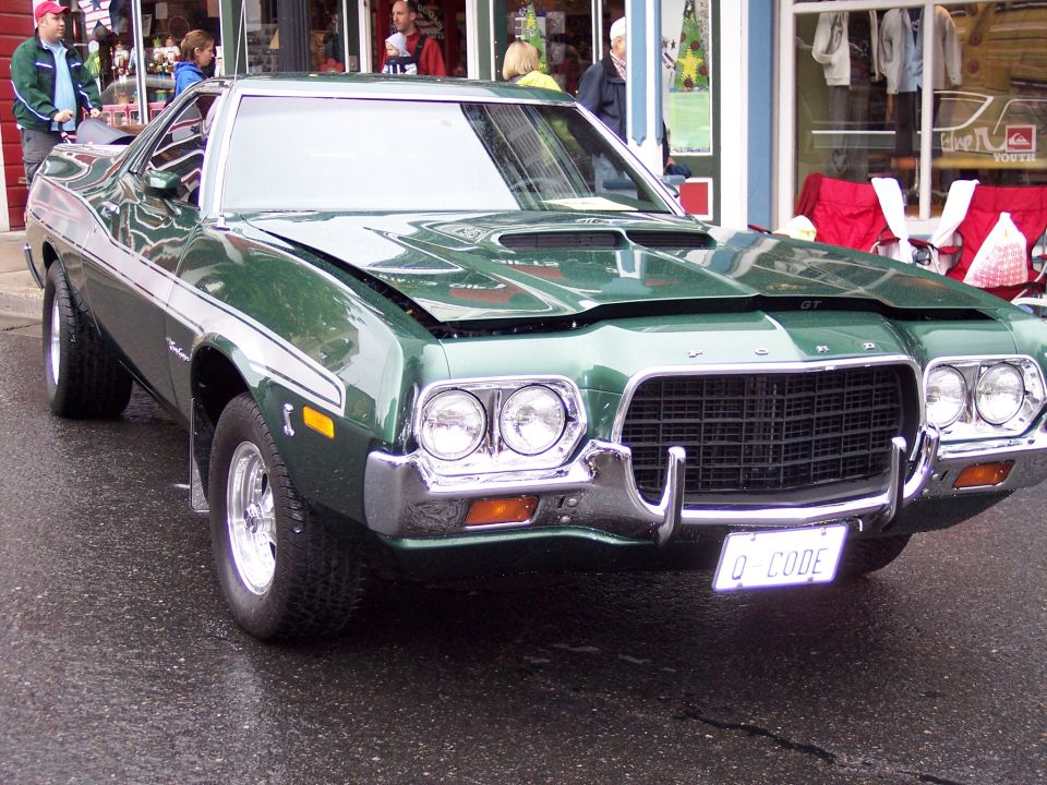 Dark green Ford with chrome grille and 'Q-CODE' plate parked on wet street.