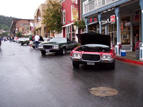 1972 Ford Ranchero - A red 1972 Ford Ranchero is parked on a wet street with its hood open, alongside other vehicles.