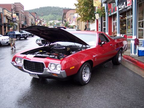 1972 Ford Ranchero - A red 1972 Ford Ranchero is parked on a wet street with its hood open, showing the engine compartment.