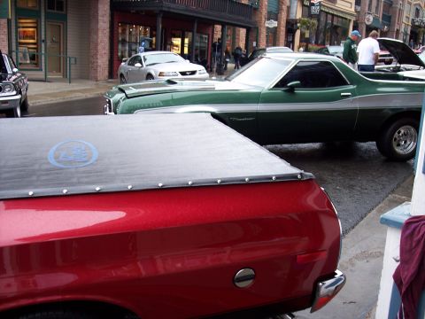 1972 Ford Ranchero - Two pickup trucks are parked on a street in front of buildings. The green one is a 1972 Ford Ranchero.