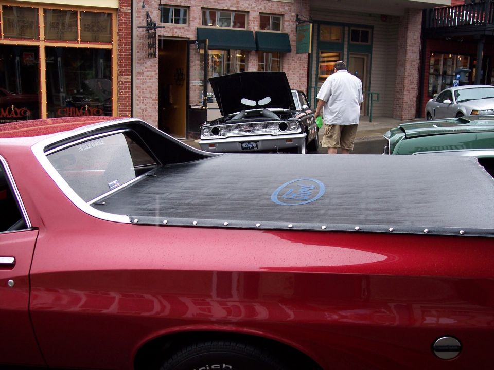 Red Ford Ranchero rear quarter with black tonneau bed cover and blue Ford logo, on a street.