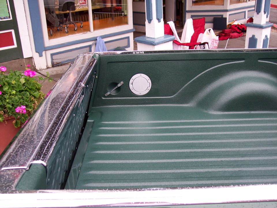 Green bedliner-coated truck bed corner with chrome fuel door and rail