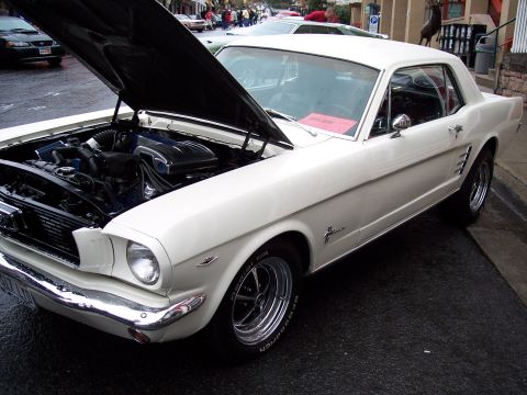 1972 Ford Ranchero - White 1965 Ford Mustang coupe parked on a wet street with hood open.