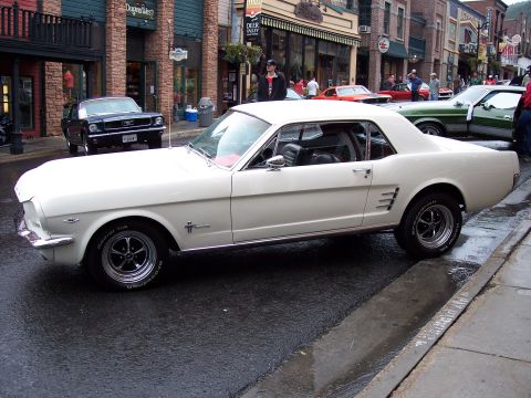 1972 Ford Ranchero - A classic white Ford Mustang is parked on a wet street, with other vehicles and storefronts visible.