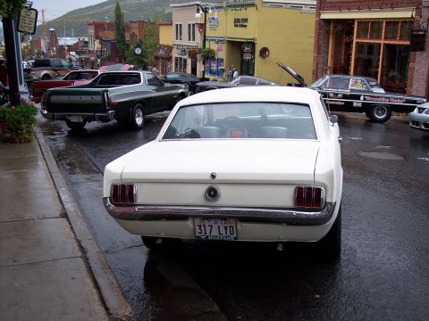 1972 Ford Ranchero - A white 1965 Ford Mustang parked on a wet street in a town.