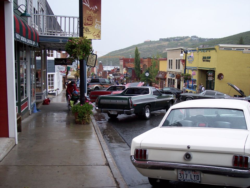 Green Ford Ranchero parked on wet street, white Mustang in foreground