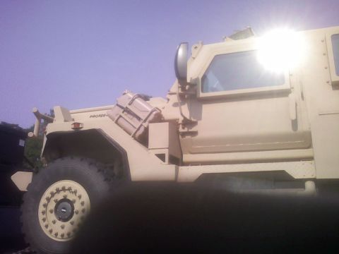 2001 Ford F-150 - Side view of a tan armored military truck with a large tire and a reinforced cab.