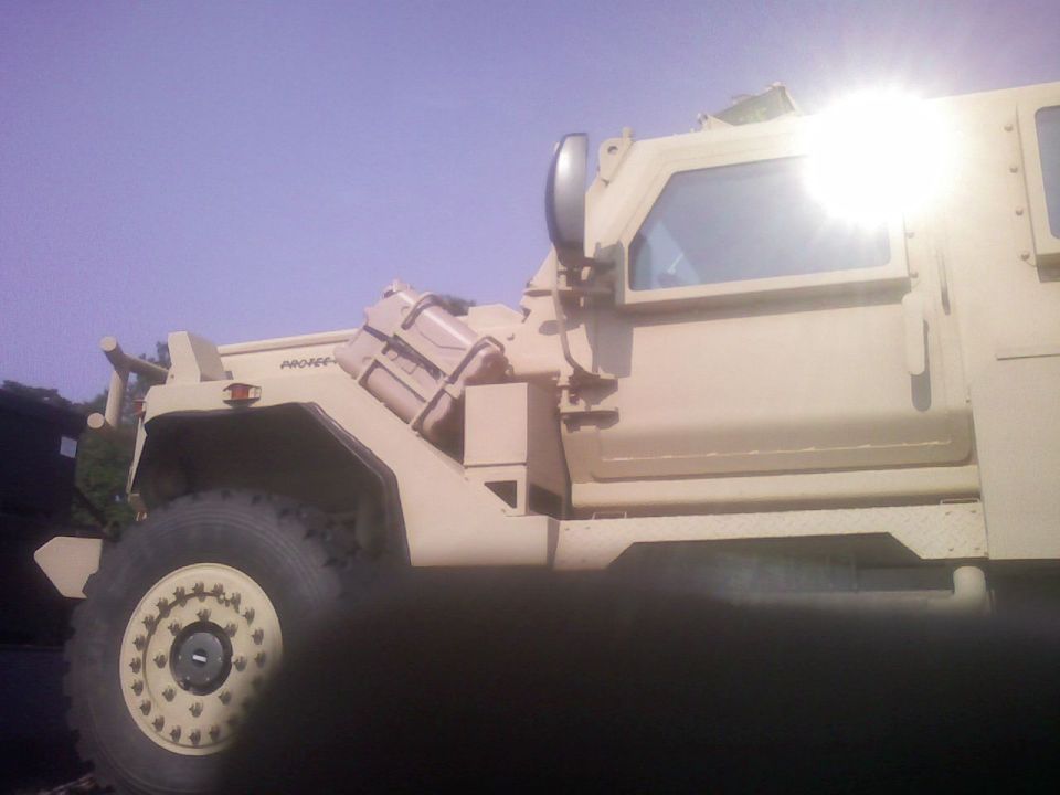 Tan military truck side view, showing large tire and armored cab