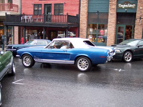 1972 Ford Ranchero - A blue 1967 convertible with white racing stripes and 'GT 500' badging is parked on a wet street.