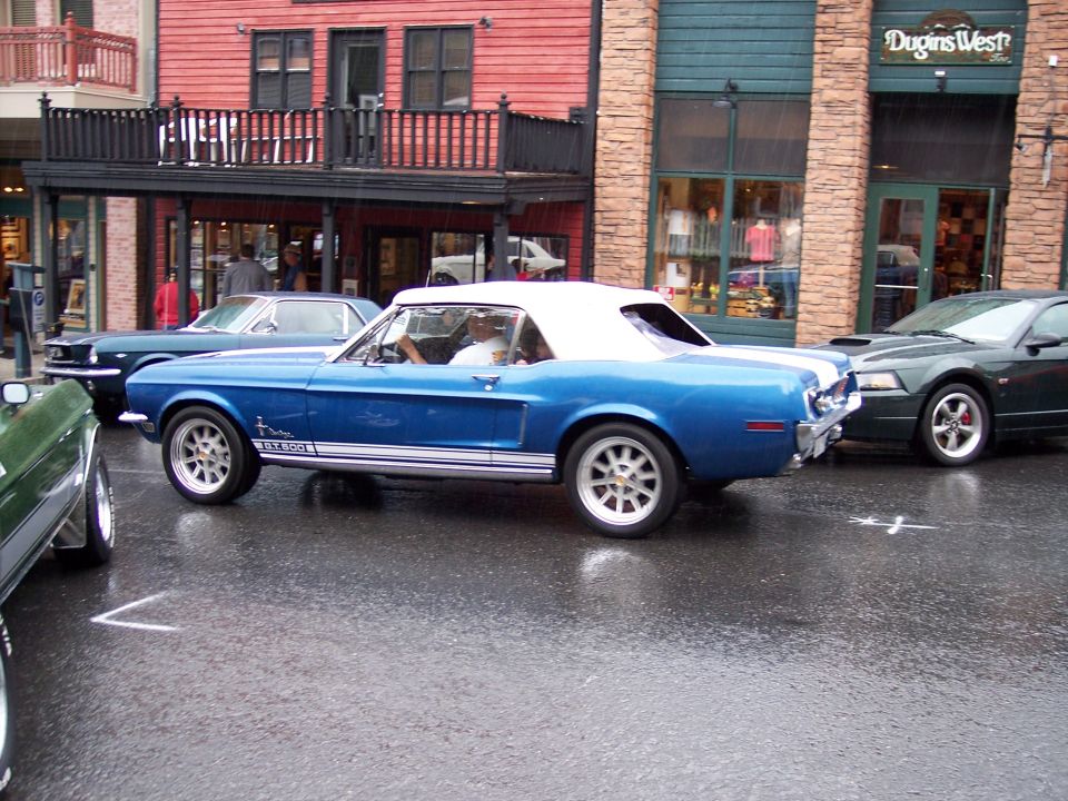 Blue vintage Mustang convertible with white top and GT 500 stripes on wet street