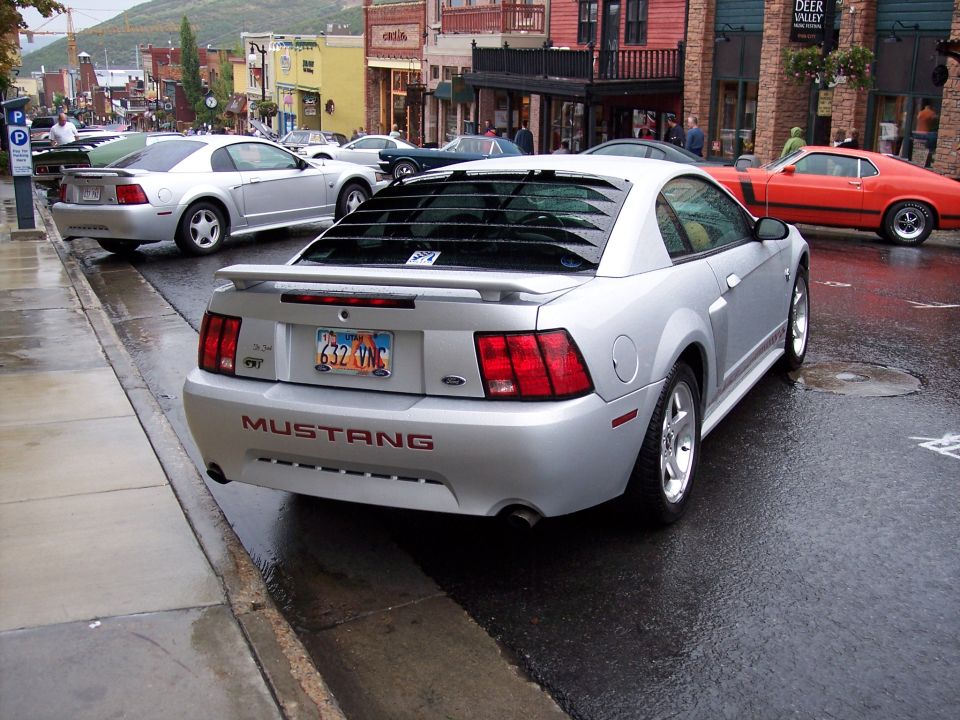 Silver Ford Mustang coupe, rear view, parked on wet city street