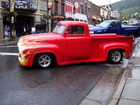 1972 Ford Ranchero - A classic red pickup truck with flame decals is parked on a wet street in front of a theater.
