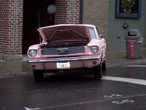 1972 Ford Ranchero - A pink 1965 Ford Mustang is parked on a wet street with its hood up.