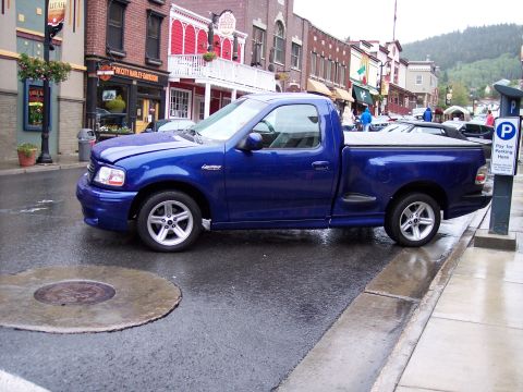 1972 Ford Ranchero - Blue Ford F-150 Lightning pickup truck parked on wet street in a town.