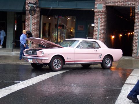 1972 Ford Ranchero - A pink 1965 Ford Mustang coupe is parked on a wet street with its hood up.