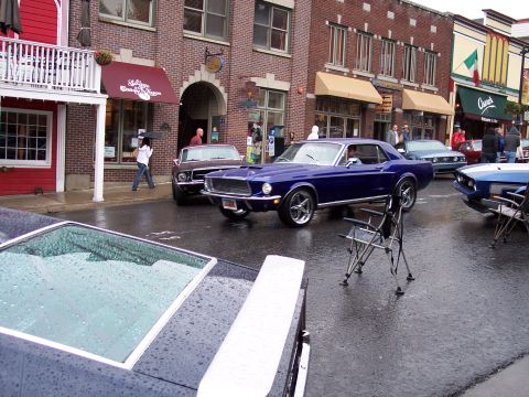 1972 Ford Ranchero - Several classic Ford Mustangs are parked on a wet street in a town square.