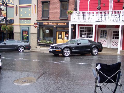 1972 Ford Ranchero - A black Ford Mustang is parked on a wet street in front of a Harley-Davidson dealership, with another car visible in the background.